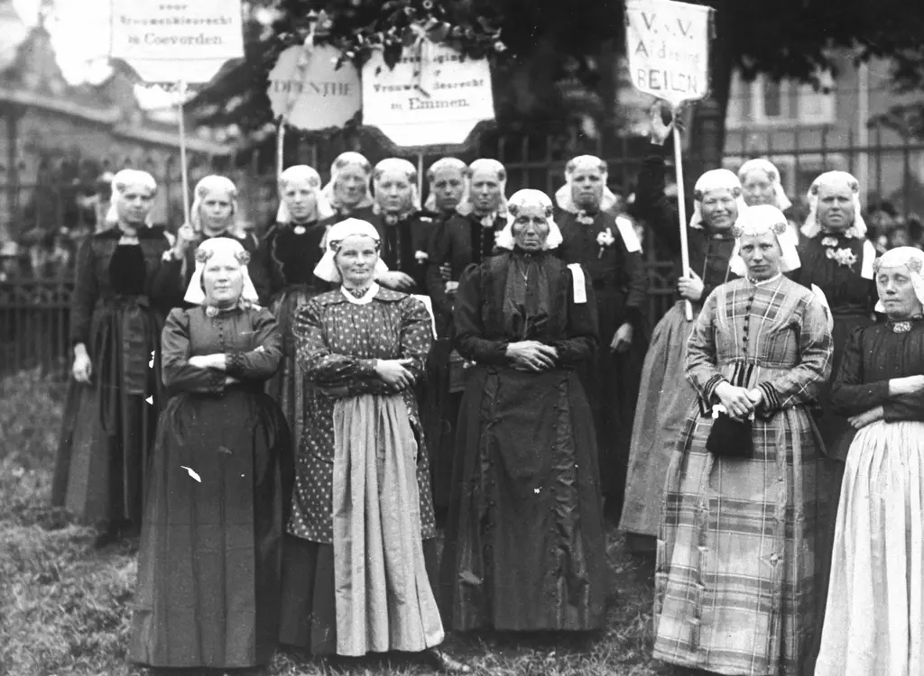 Groep vrouwen in klederdracht waarvan een aantal borden en vaandels in de hand omhoog houden.