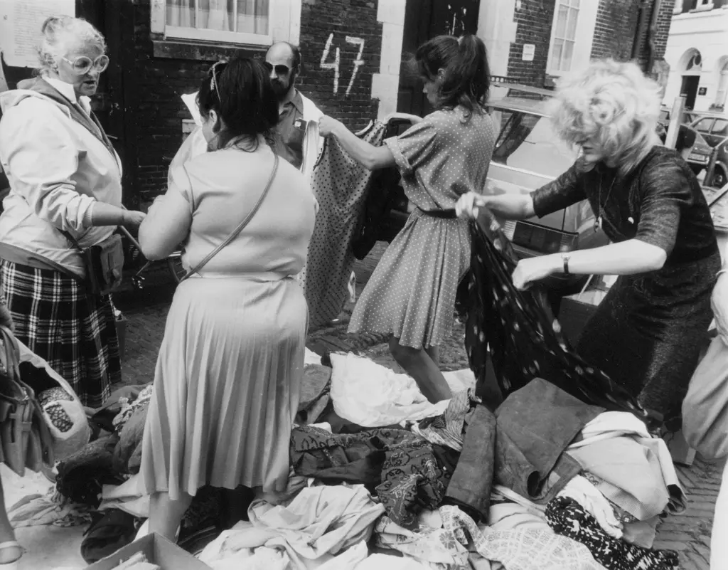 Groep mensen zoekt door een berg tweedehands kleding