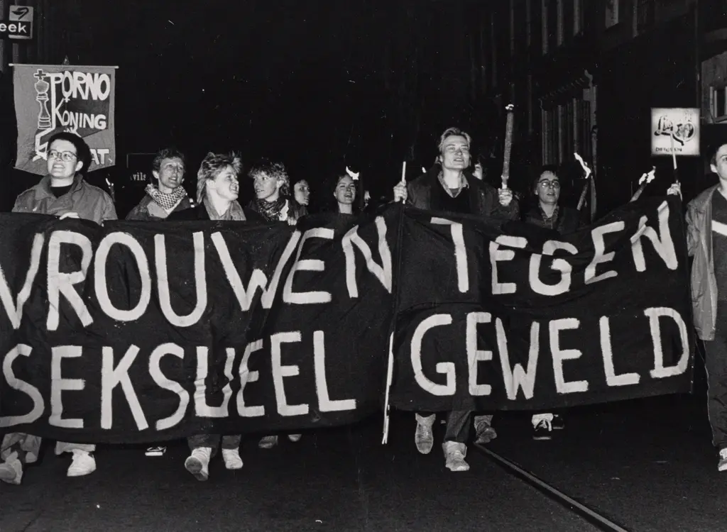 Groep vrouwen met fakkels in de hand lopen achter groot spandoek met tekst Vrouwen tegen seksueel geweld