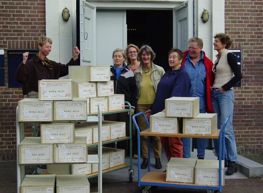 Aantal IAV-medewerkers staan lachend voor de deuropening met voor zich twee bibliotheekkarren met archiefdozen met Russische labels 