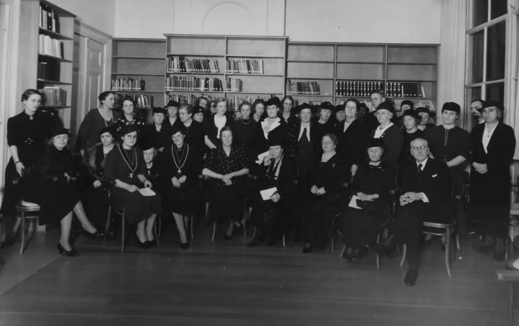 Groep mensen zittend en staand voor een aantal boekenkasten, met o.a. het bestuur van het IAV
