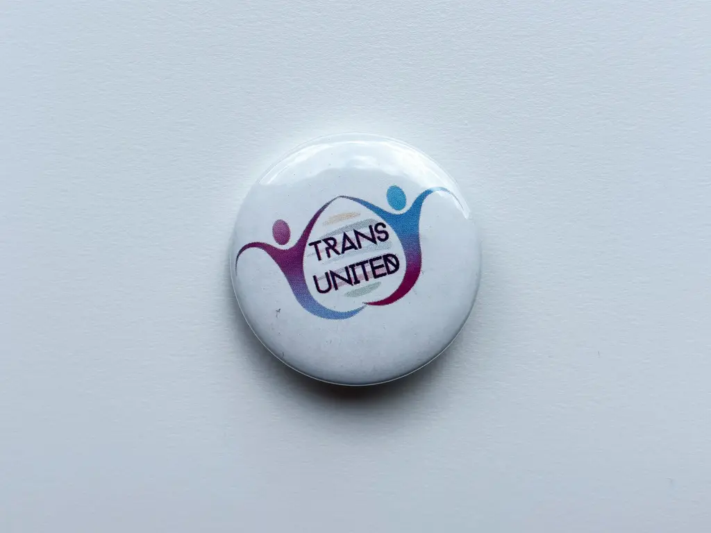 Witte button met 2 symbolische figuren die met elkaar verbonden zijn en tekst Trans United