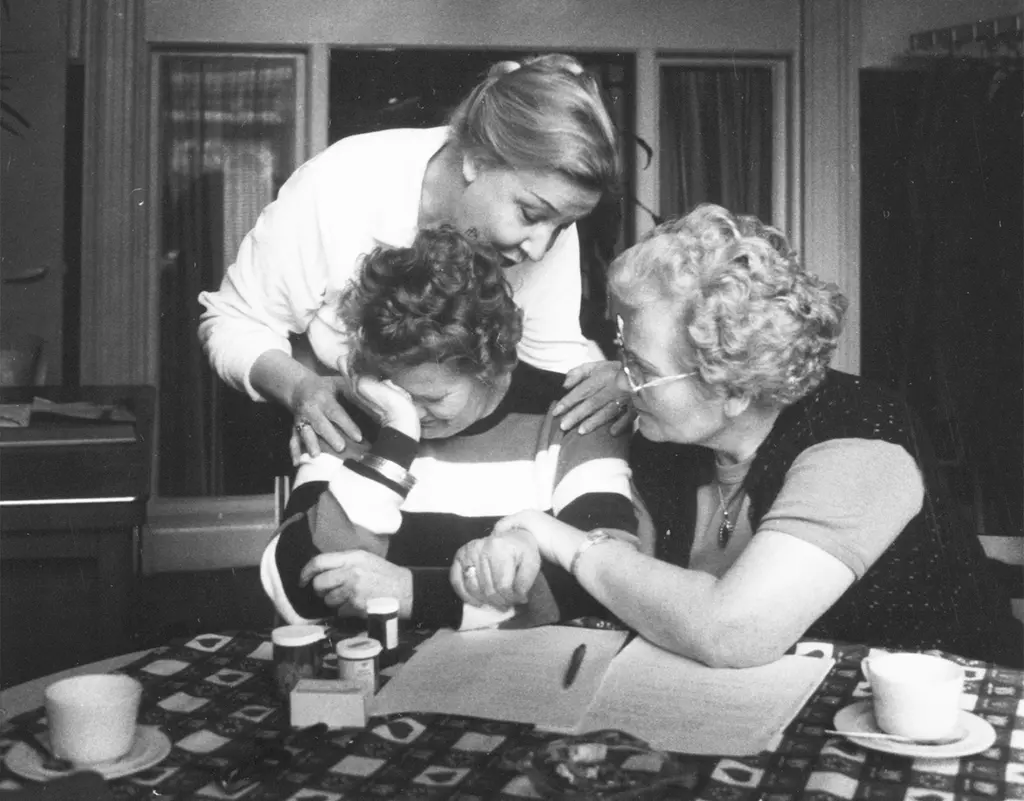 Twee vrouwen troosten een vrouw die aan tafel zit