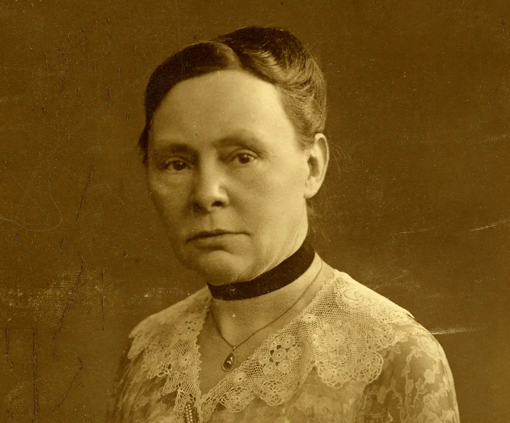 Portret in sepia van ernstig kijkende vrouw met opgestoken haar met om haar nek een bandje