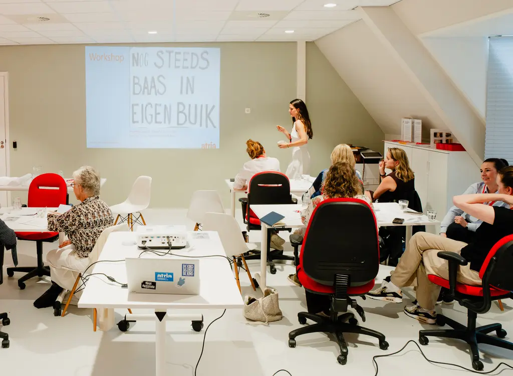Groepjes deelnemers in gesprek met elkaar met op de achtergrond de tekst Workshop Nog steeds baas in eigen buik
