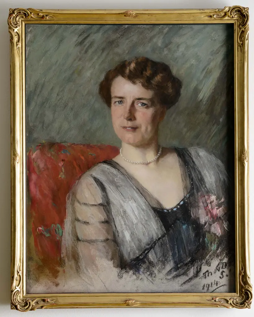 Vrouw met kort krullend haar in blauwe jurk zittend op een rode stoel