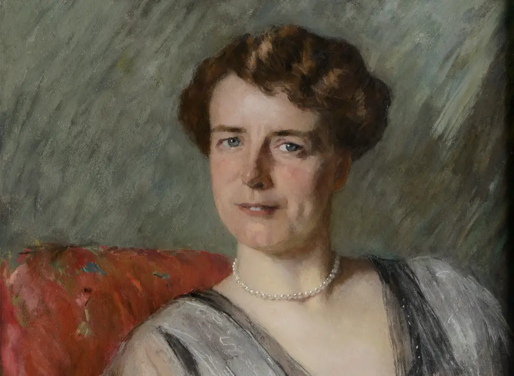 Vrouw met kort krullend haar in blauwe jurk zittend op een rode stoel